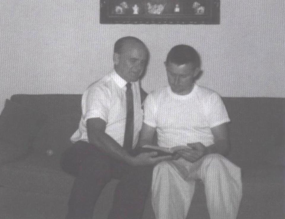 William Branham (left) sitting closely with another male associate, holding his hand on the man's lap, indoor couch setting