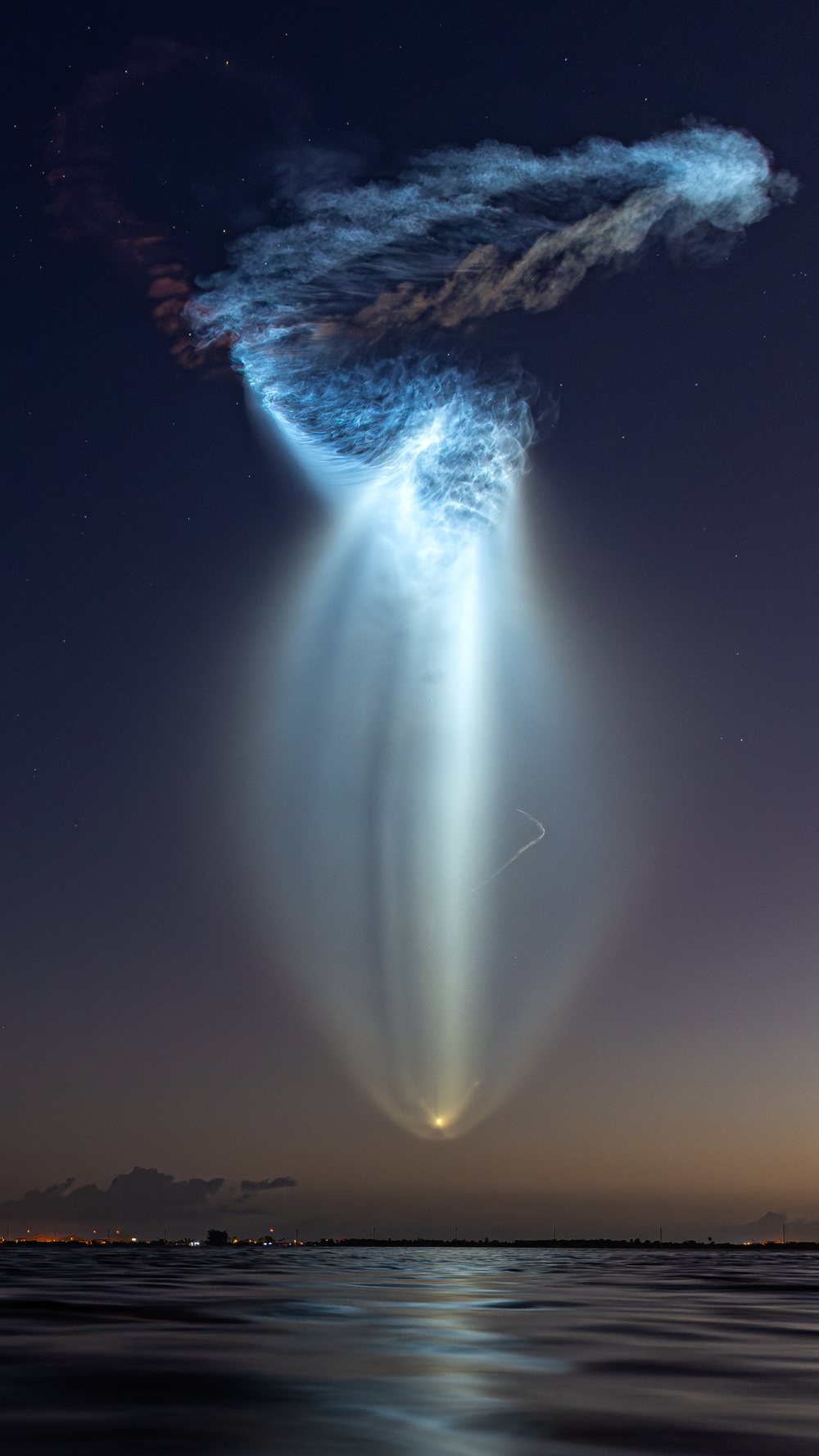 A towering SpaceX Falcon 9 launch plume billowing into a luminous cloud before dawn
